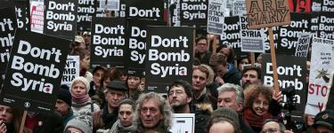 A demonstration in which many people are holding "Don't Bomb Syria" placards, and one placard says "We are many".