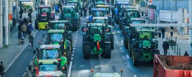 Three rows of green tractors make their way through a busy high street during a protest.