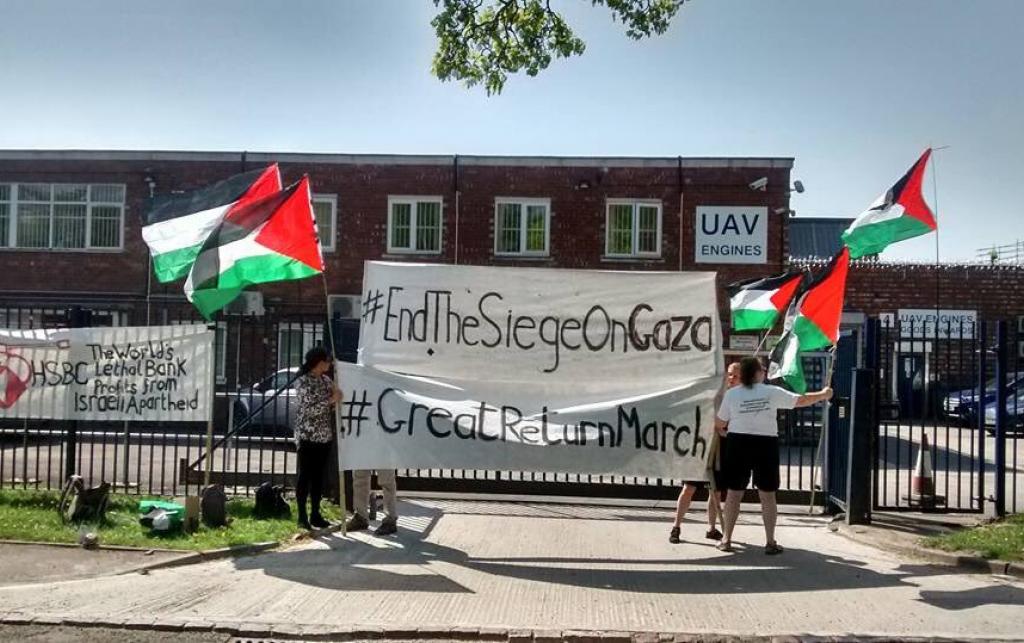 Stop Arming Israel campaigners take action outside an Elbit-owned factory in Birmingham. Photo: Birmingham Palestine Action. They are flying Palestine flags. A banner on the fence outside the factory reads "HSBC: The World's Lethal Bank profits from Israeli Apartheid. The protesters hold another banner that reads "#EndTheSeigeOnGaza #GreatReturnMarch"