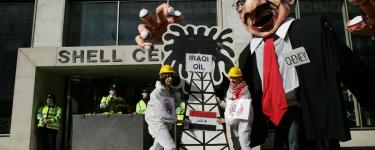 Hands Off Iraqi Oil demo, 2008. Activists dressed as oil industry workers are outside of a Shell building, with a model of an oil drilling rig labelled "Iraqi oil", in front of a large caricature model labelled "Chaney".
