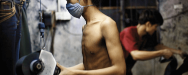 A worker sandblasts denim at a factory, topless but wearing a facemask. Photo: Justin Jin / Panos Pictures