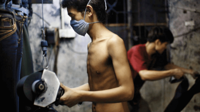 A worker sandblasts denim at a factory, topless but wearing a facemask. Photo: Justin Jin / Panos Pictures