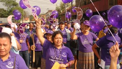 Women workers who are members of Codemuh take part in a street demonstration, wearing purple and holding purple balloons.