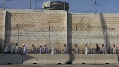 Palestinian workers in Israel protest dehumanising conditions at checkpoints. A queue of people stand in a line in front of a tall wall at a checkpoint. Source: Wikipedia